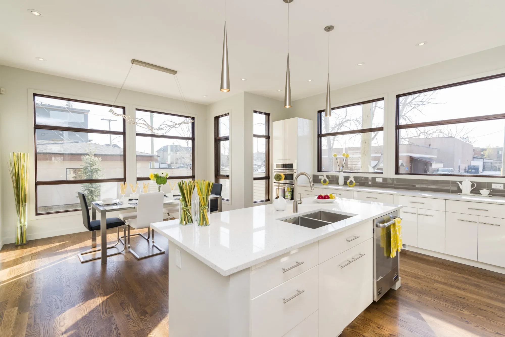 White kitchen island with a double sink beside a sunlit dining area