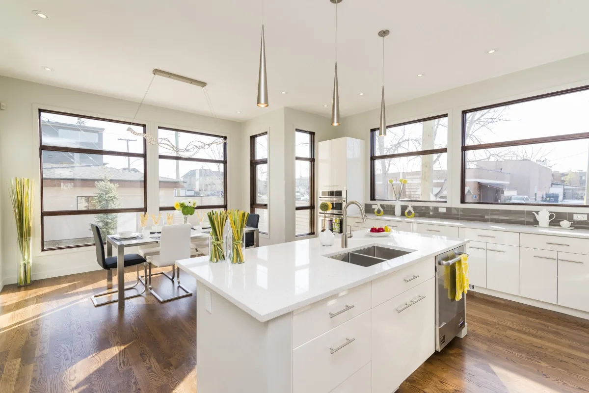 White kitchen island with a double sink beside a sunlit dining area