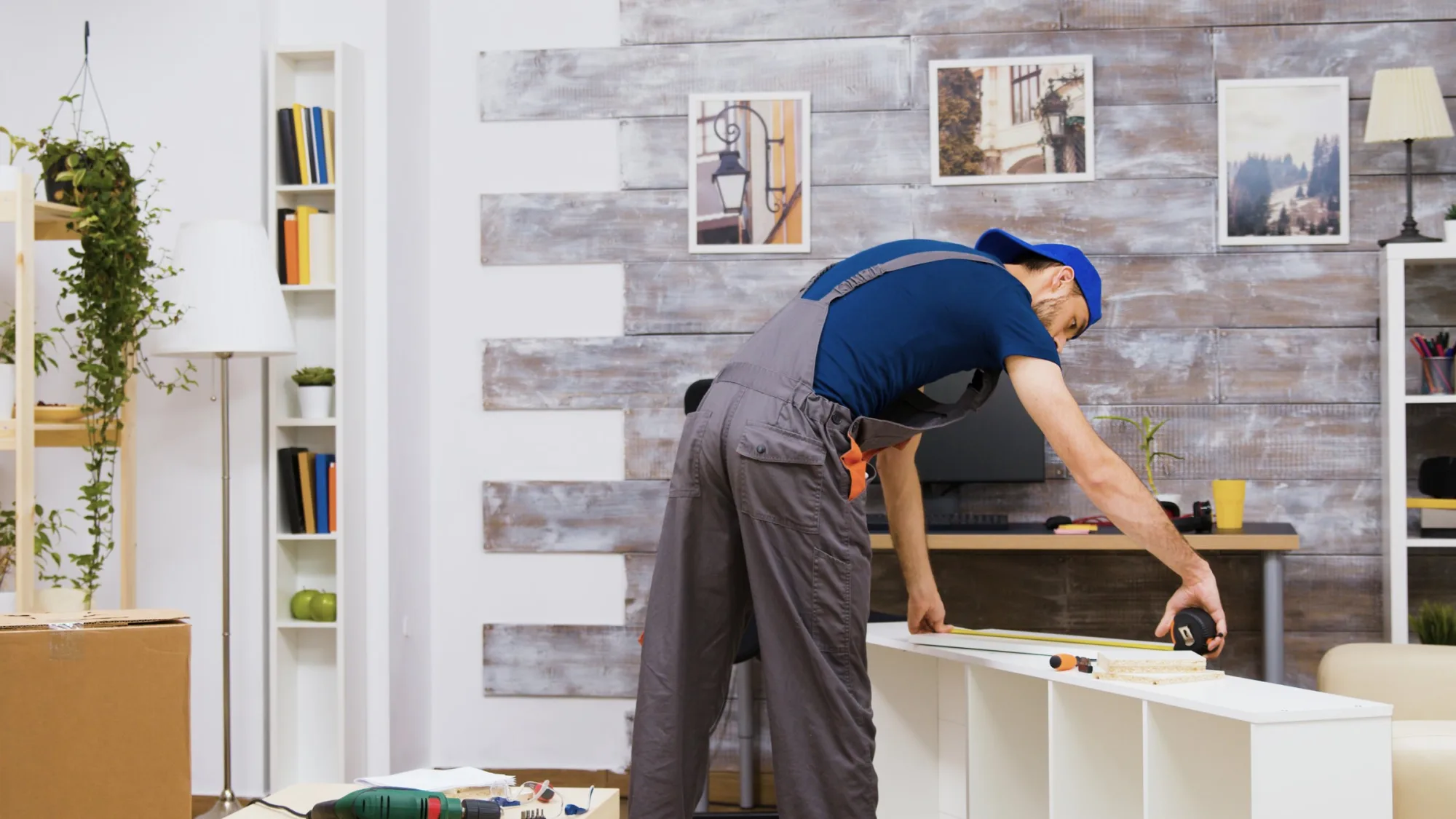 Installer measuring a white shelving unit in a living room with a whitewashed timber feature wall